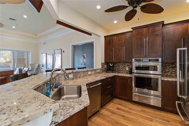 kitchen featuring appliances with stainless steel finishes, light stone counters, crown molding, sink, and light hardwood / wood-style floors