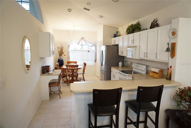 kitchen with kitchen peninsula, white appliances, vaulted ceiling, and a kitchen bar