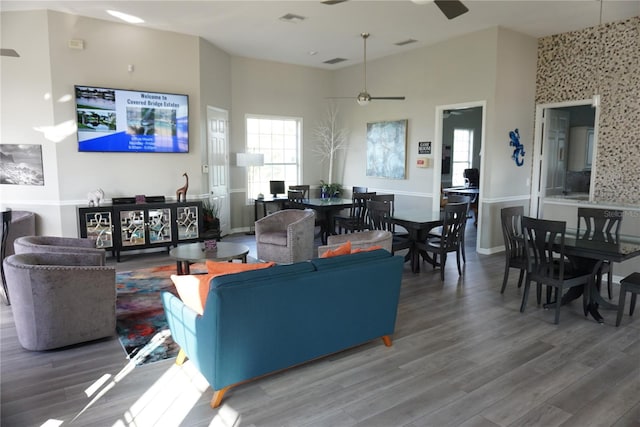 living room with wood-type flooring, ceiling fan, and a towering ceiling