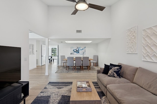 living room with a towering ceiling, a skylight, ceiling fan, and light hardwood / wood-style floors