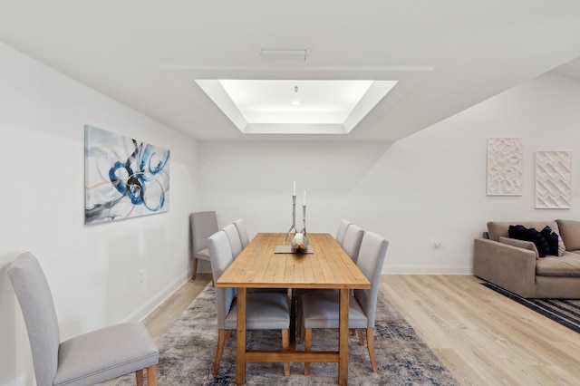 dining space with light hardwood / wood-style floors, a raised ceiling, and a skylight