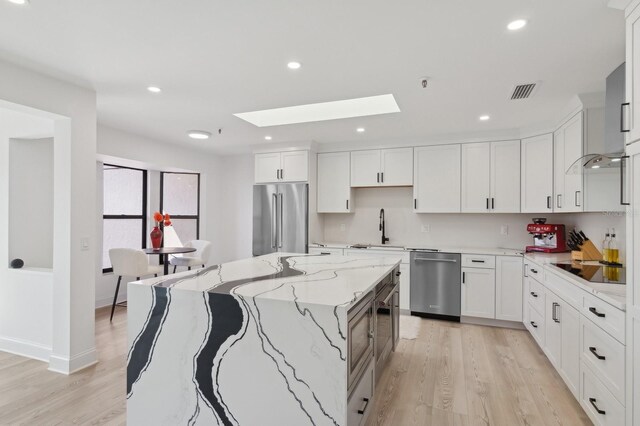 kitchen with a center island, a skylight, light stone counters, white cabinetry, and stainless steel appliances