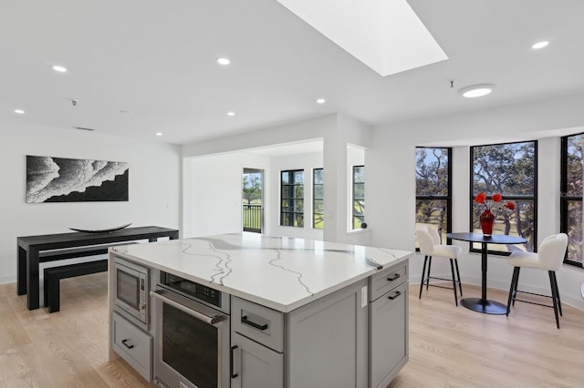 kitchen featuring stainless steel appliances, gray cabinets, light hardwood / wood-style floors, and light stone counters