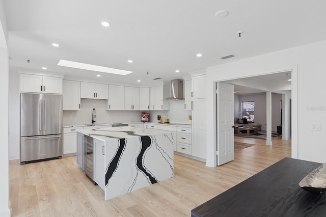 kitchen featuring high quality fridge, light hardwood / wood-style flooring, a kitchen island, and wall chimney range hood