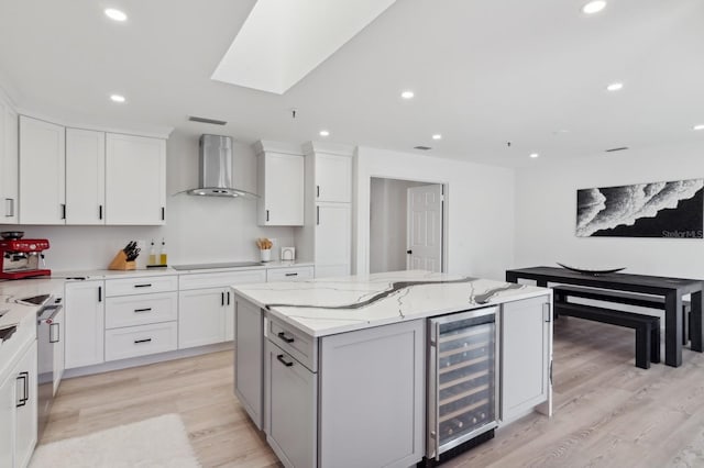 kitchen with a center island, white cabinets, wine cooler, wall chimney exhaust hood, and light wood-type flooring