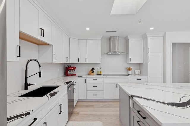 kitchen featuring white cabinets, sink, light hardwood / wood-style flooring, wall chimney exhaust hood, and light stone countertops