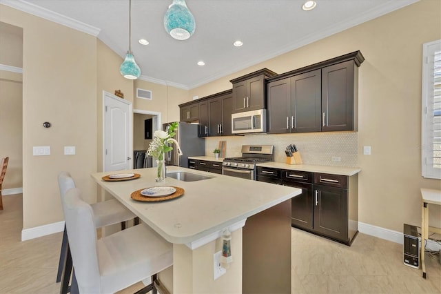 kitchen with a kitchen bar, ornamental molding, stainless steel appliances, pendant lighting, and an island with sink