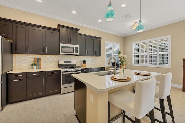 kitchen featuring sink, hanging light fixtures, stainless steel appliances, a center island with sink, and ornamental molding