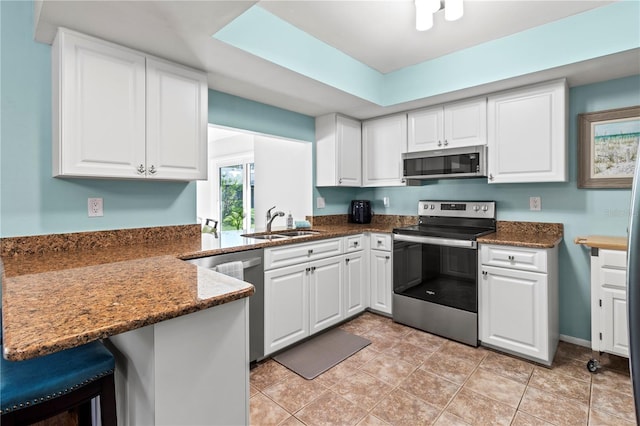 kitchen featuring dark stone counters, sink, kitchen peninsula, appliances with stainless steel finishes, and white cabinetry