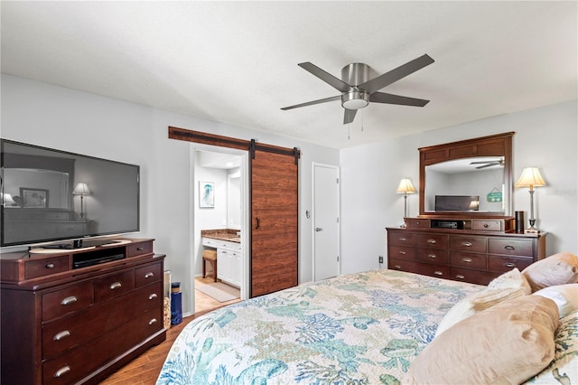 bedroom featuring ceiling fan, a barn door, light wood-type flooring, and connected bathroom