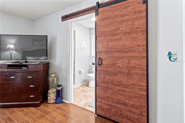 bedroom featuring connected bathroom, a barn door, and light wood-type flooring