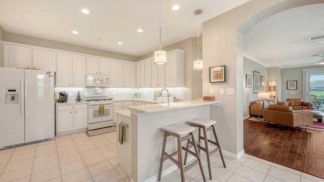 kitchen with light hardwood / wood-style floors, kitchen peninsula, decorative light fixtures, white appliances, and white cabinets