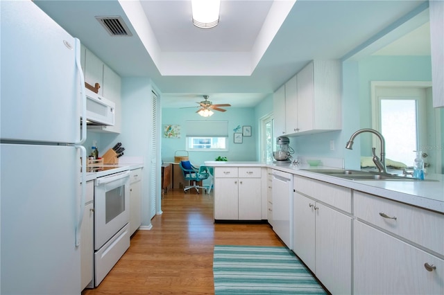 kitchen with a raised ceiling, kitchen peninsula, white appliances, white cabinets, and light wood-type flooring