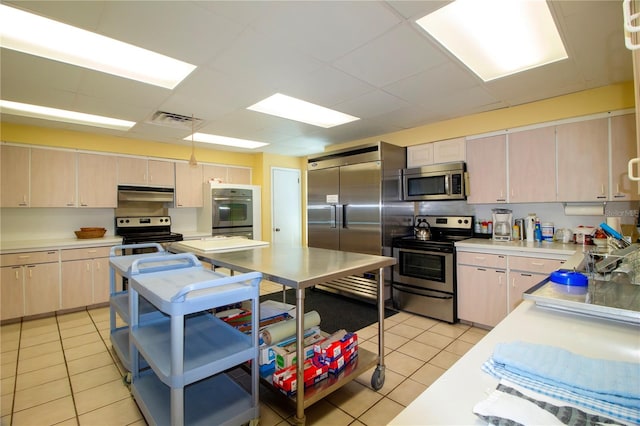 kitchen with light brown cabinets, stainless steel appliances, light tile patterned floors, and pendant lighting