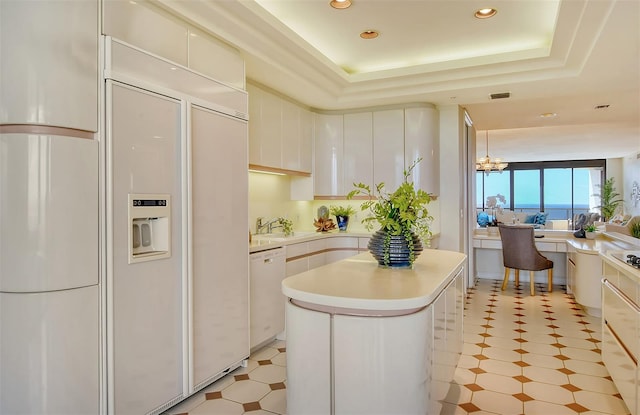 kitchen with white cabinetry, a notable chandelier, a raised ceiling, white appliances, and a center island