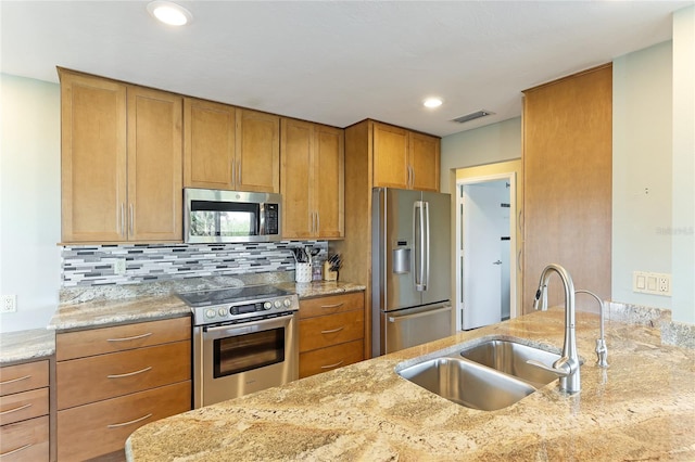 kitchen with appliances with stainless steel finishes, sink, light stone counters, and backsplash