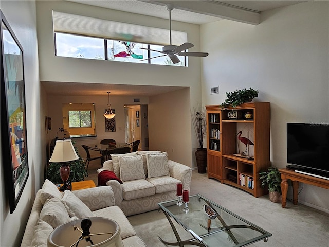 living room with a wealth of natural light, ceiling fan, light carpet, and a high ceiling