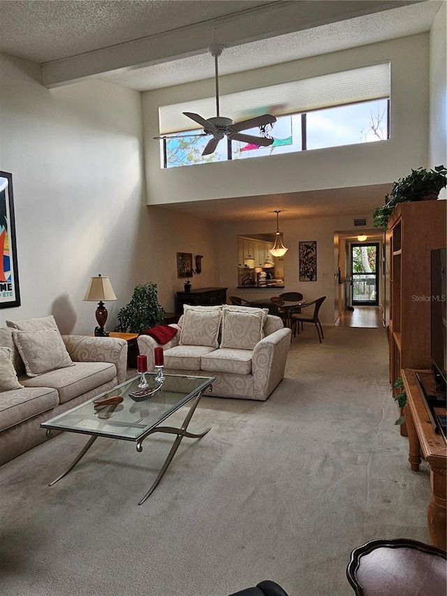 living room with a high ceiling, ceiling fan, a textured ceiling, beamed ceiling, and carpet floors