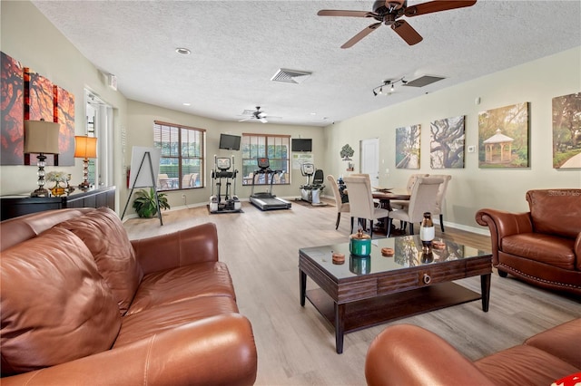 living room with light wood finished floors, visible vents, a textured ceiling, and ceiling fan