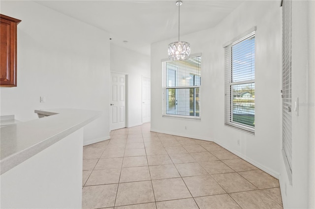 unfurnished dining area with light tile patterned floors, baseboards, and a chandelier