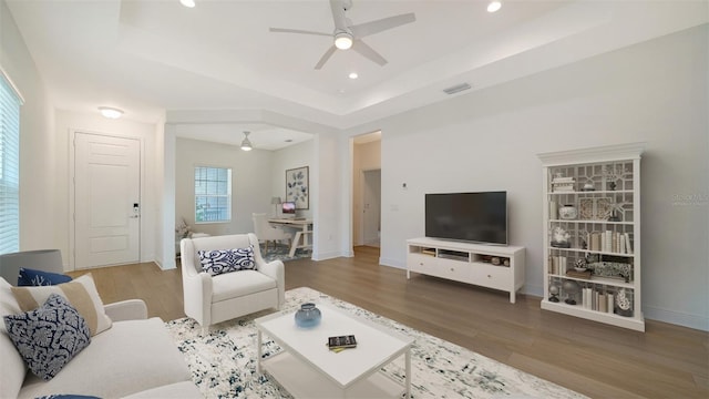 living room featuring hardwood / wood-style floors, ceiling fan, and a tray ceiling