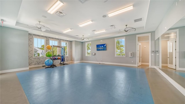 exercise room featuring a raised ceiling, a wealth of natural light, and ceiling fan