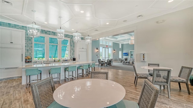 interior space with white cabinetry, light wood-type flooring, decorative light fixtures, a kitchen bar, and ornamental molding