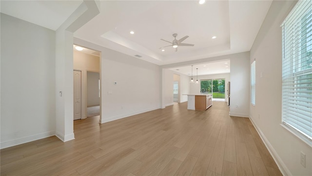 unfurnished living room featuring ceiling fan, a raised ceiling, and light hardwood / wood-style floors