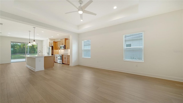 kitchen featuring sink, stainless steel appliances, hanging light fixtures, light hardwood / wood-style flooring, and an island with sink