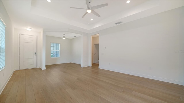 unfurnished room with light hardwood / wood-style flooring, ceiling fan, and a tray ceiling