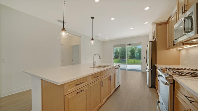 kitchen featuring sink, stainless steel appliances, pendant lighting, light hardwood / wood-style floors, and a kitchen island with sink