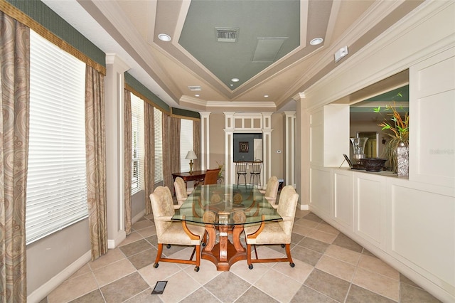 tiled dining area with a tray ceiling, a wealth of natural light, decorative columns, and ornamental molding