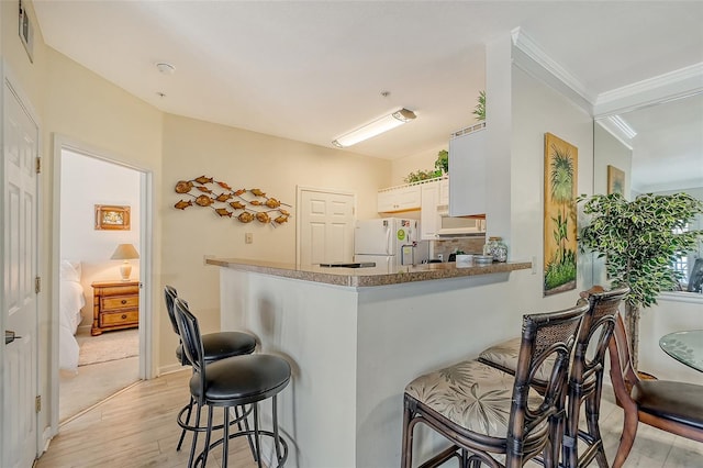 kitchen featuring a breakfast bar, white cabinetry, crown molding, kitchen peninsula, and white appliances