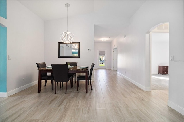 dining area with an inviting chandelier, light wood-type flooring, and vaulted ceiling