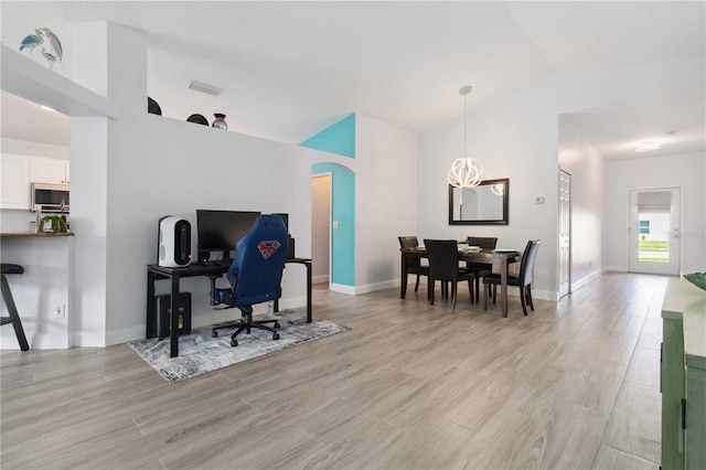 office area with light hardwood / wood-style floors, lofted ceiling, and an inviting chandelier