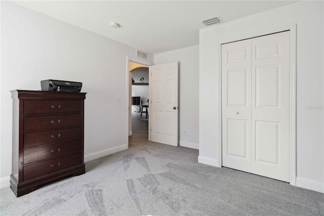 bedroom featuring light carpet, a textured ceiling, and a closet