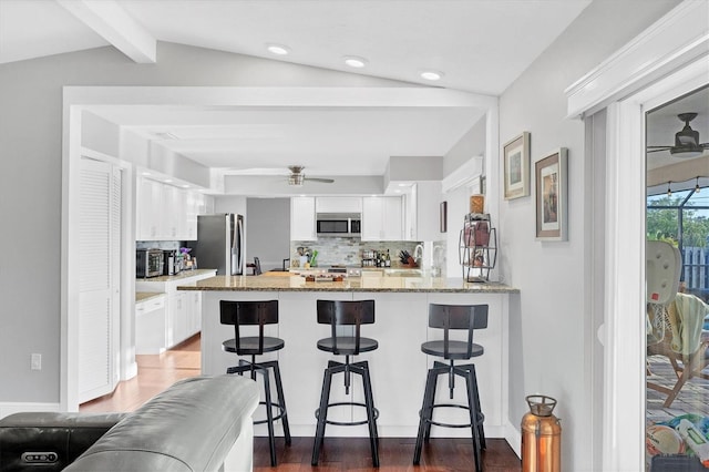 kitchen with white cabinets, decorative backsplash, vaulted ceiling with beams, light stone countertops, and stainless steel appliances