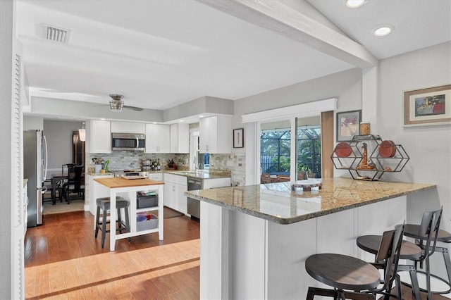 kitchen with kitchen peninsula, light wood-type flooring, light stone counters, stainless steel appliances, and white cabinetry