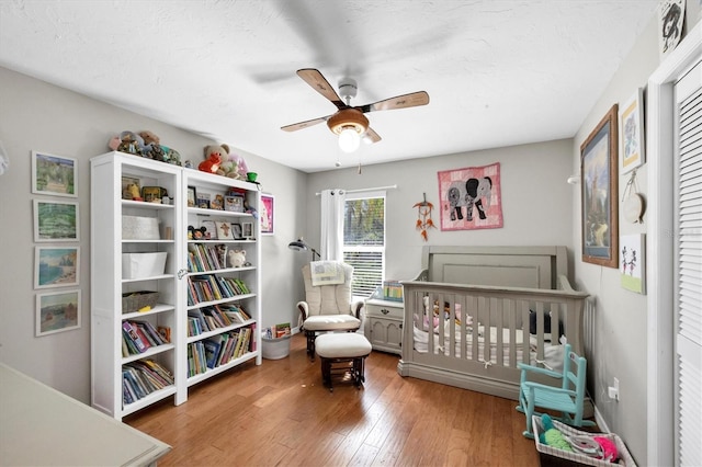 bedroom featuring ceiling fan, wood-type flooring, and a crib