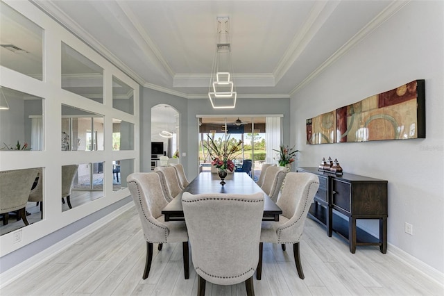 dining space with a raised ceiling, ornamental molding, and light hardwood / wood-style flooring