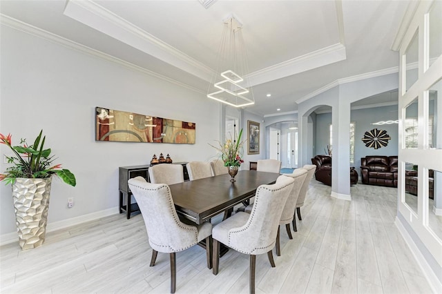 dining space with a tray ceiling, a notable chandelier, light hardwood / wood-style flooring, and ornamental molding