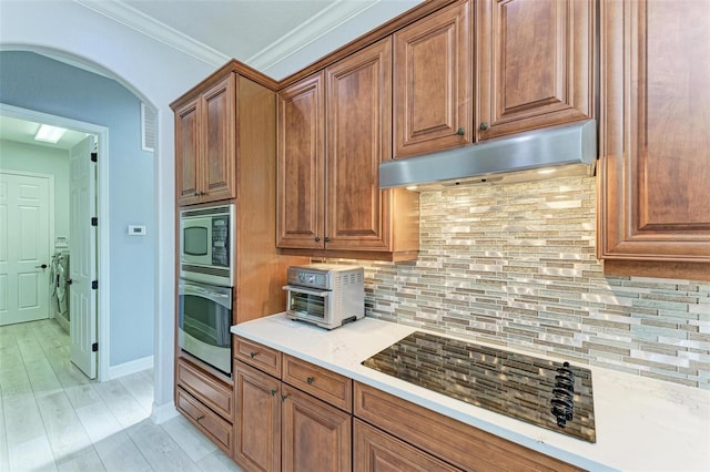 kitchen with stainless steel appliances, ornamental molding, light hardwood / wood-style flooring, and backsplash