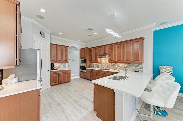 kitchen with light wood-type flooring, appliances with stainless steel finishes, a kitchen bar, sink, and kitchen peninsula