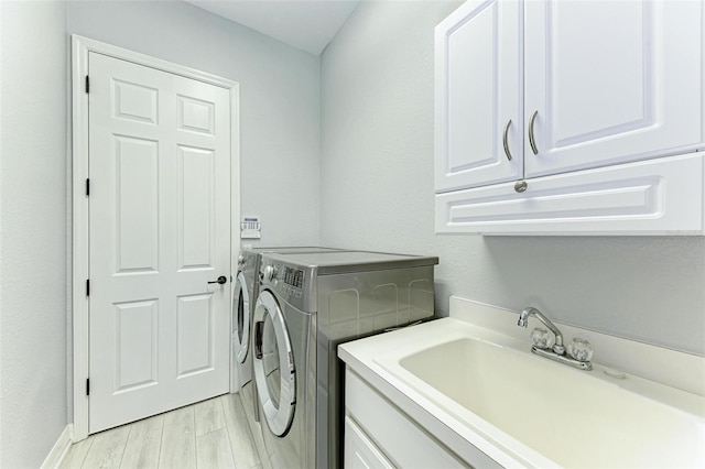 laundry room with light hardwood / wood-style flooring, washing machine and dryer, cabinets, and sink