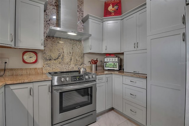 kitchen with wall chimney range hood, tasteful backsplash, light stone counters, stainless steel electric stove, and light tile patterned floors