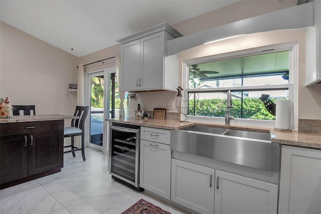 kitchen with light stone countertops, sink, beverage cooler, and vaulted ceiling