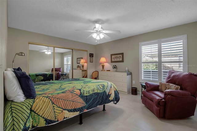 bedroom with a textured ceiling, ceiling fan, multiple windows, and a closet