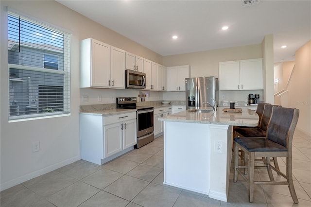 kitchen with a center island with sink, white cabinetry, appliances with stainless steel finishes, light stone countertops, and sink