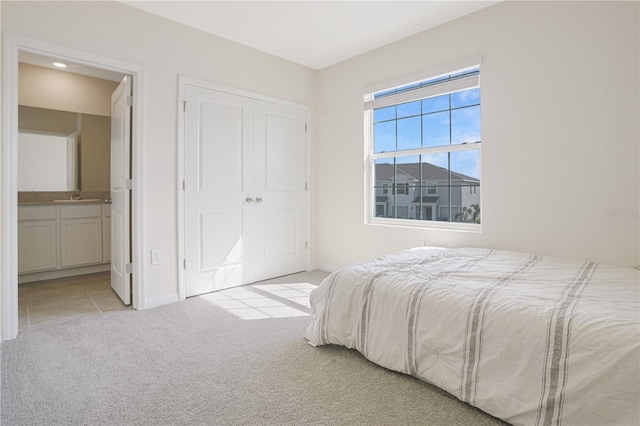 bedroom featuring ensuite bathroom, light colored carpet, sink, and a closet