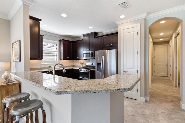 kitchen featuring kitchen peninsula, light stone counters, stainless steel appliances, crown molding, and a breakfast bar area